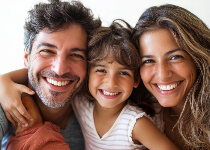 A cheerful family of four, all smiling widely, with parents and kids